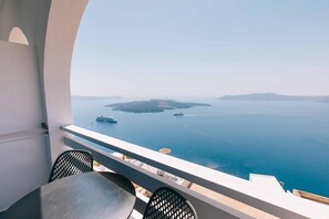 A balcony with a table and chairs overlooking a calm sea with boats and islands. - Kafieris View (Santorini)