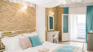 A bedroom with a bed, bedside table, and a desk. There is a window with curtains and a view of the outside. - Kafieris View (Santorini)
