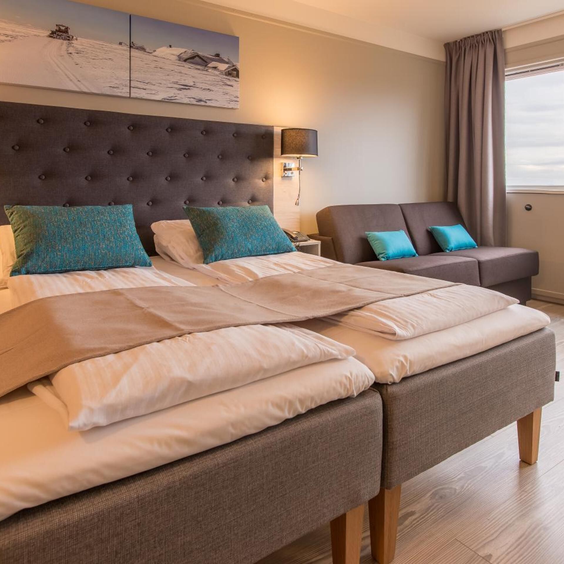 A hotel room with a large bed, a sofa, a wall-mounted lamp, and a painting above the bed.