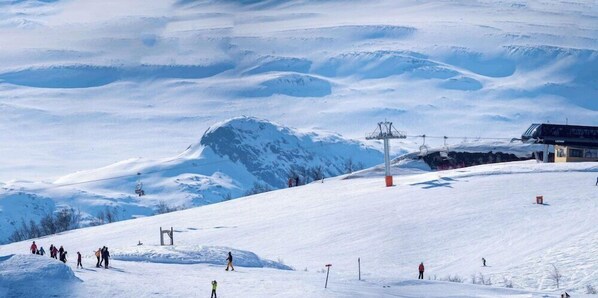 A snowy ski slope with a ski lift, a mountain peak, and a building with a sloped roof. - Radisson Blu Resort Beitostolen (Øystre Slidre)