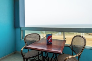 A table with a bag of OYO branded snacks, two wicker chairs, and a view of the beach through a window. - Mermaid Beach Hotel (Ajman)
