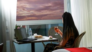 A person sitting at a table with a laptop, a sandwich, a glass of drink, and a water bottle.