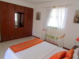 Un dormitorio con cama, armario, ventana con cortinas y un cuadro en la pared.