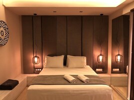 A modern bedroom with a large bed, two bedside lamps, and a decorative wall piece.
