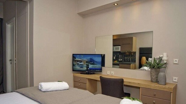 A hotel room with two beds, a desk, a television, and a mirror. - Ionian Eye (Corfu)