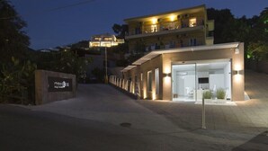 A modern hotel with a well-lit entrance, a visible signboard, and a multi-story building in the background. - Ionian Eye (Corfu)