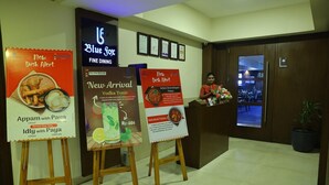 A hotel reception area with three promotional posters for dishes, a neon sign for 'Blue Fox Fine Dining', and a receptionist at the counter.