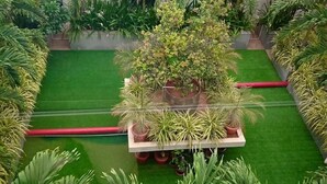 A courtyard with a central planter, surrounded by various potted plants and a green lawn.