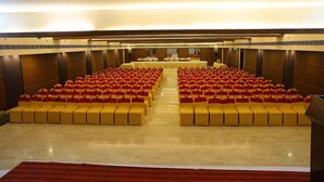 A large conference room with rows of yellow chairs and tables, a polished floor, and a high ceiling.