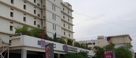 A multi-story building with balconies, a parking area, and several flags.