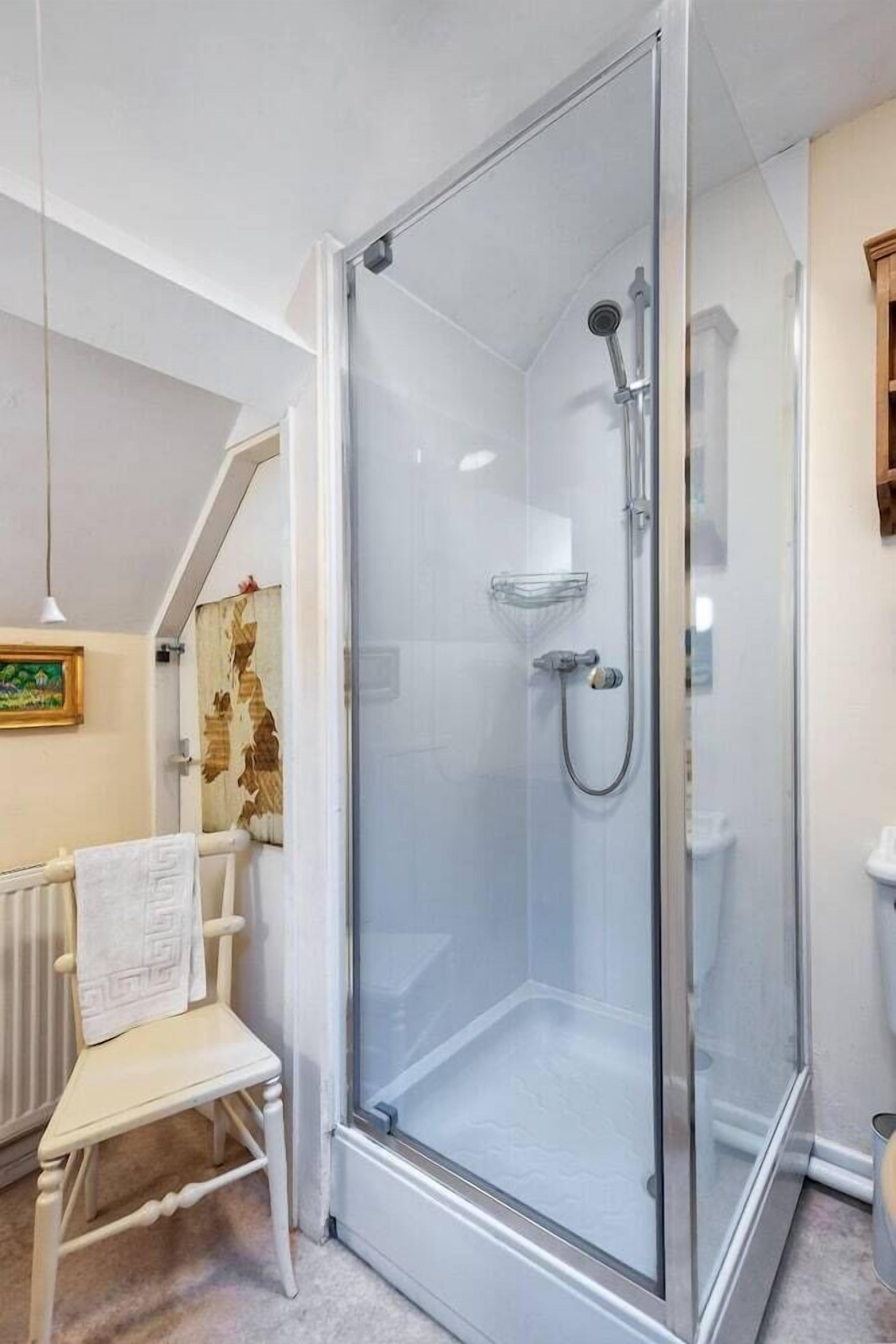 A glass-enclosed shower with a handheld showerhead and a wall-mounted faucet.