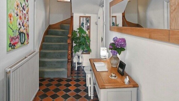 Un couloir avec un sol à carreaux, un escalier, un bureau avec un miroir et un radiateur.