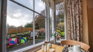 Un coin repas avec une table dressée pour deux personnes, une fenêtre donnant sur un jardin et une lampe décorative.