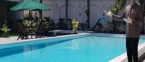 A pool area with a lifeguard, lounge chairs, and a slide.