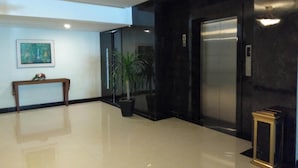 A lobby with a polished floor, a wooden bench, a potted plant, an elevator, and a framed picture on the wall. - Kawana Hotel (Padang)