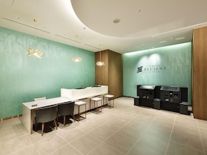 A modern hotel reception area with a teal wall, a reception desk, and a seating area with chairs. - Hotel Elcient Osaka (Osaka)
