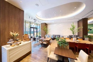 A modern hotel lobby with a reception desk, seating area, and large windows offering a view of the outside. - Hotel Elcient Osaka (Osaka)