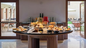 Une table de buffet proposant divers plats, une porte vitrée donnant sur un espace extérieur aménagé pour prendre les repas, et une vue sur l’espace extérieur où l’on peut dîner.