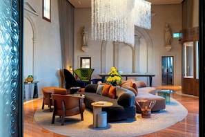 Um hall amplo com um sofá moderno, cadeiras, uma mesinha e um lustre decorativo.