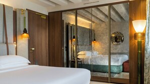 Une chambre d’hôtel avec un grand lit, une armoire, un miroir et une lampe fixée au mur.