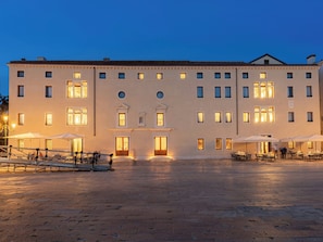 A large building with multiple windows and doors, outdoor seating with umbrellas, and a paved courtyard. - Ca di Dio (Venice)