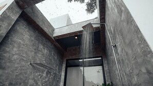Une salle de bain moderne avec un mur en béton, une porte en verre et une douche dont on peut voir le jet d’eau.