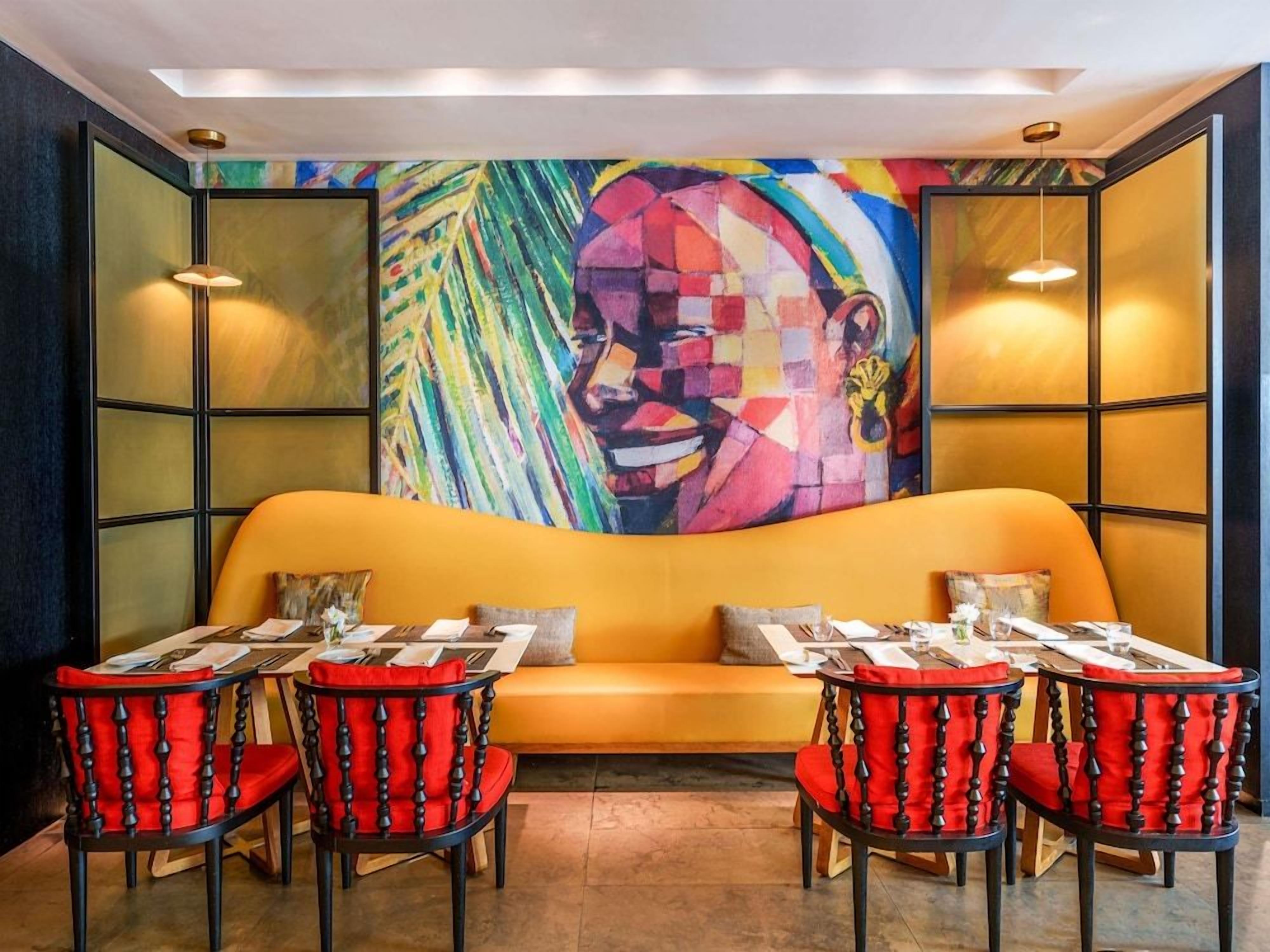 Un restaurante con un mural llamativo, asientos anaranjados y sillas rojas.