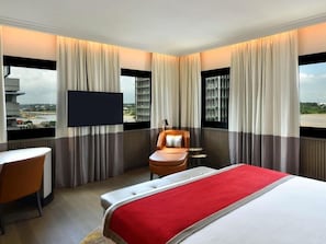 Een hotelkamer met een bed, een televisie, een stoel en uitzicht op een stadsgezicht.