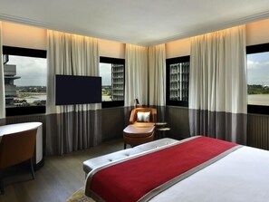 Een hotelkamer met een bed, een bureau, een stoel, een televisie en grote ramen met gordijnen.