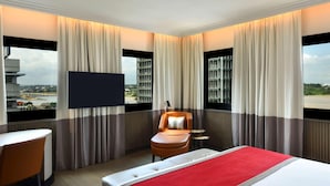 A hotel room with a bed, a chair, a TV, and a view of a bridge and buildings.