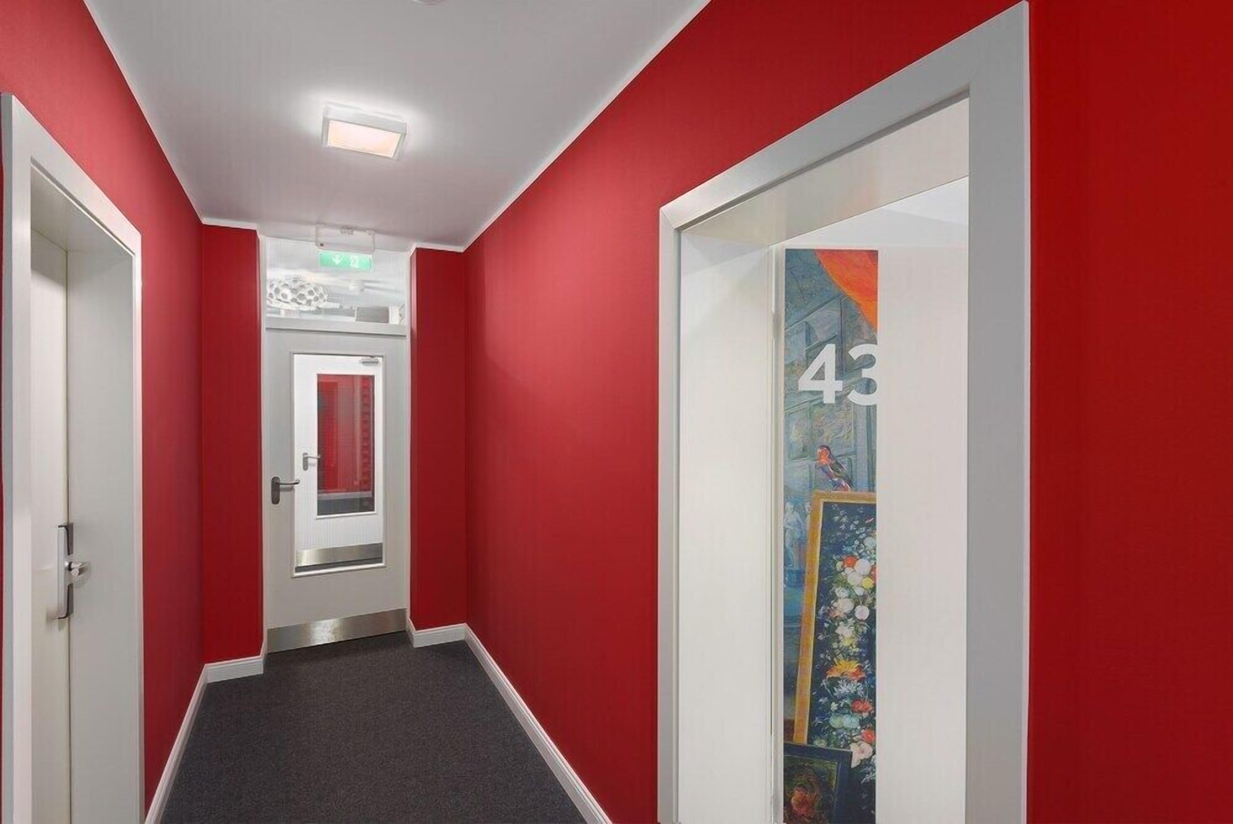 A hallway with red walls and a grey carpet. There is a door with a red curtain and a number 43 on the wall.