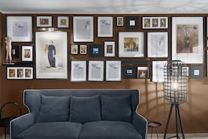 Ein Zimmer mit grauem Sofa, einer Stehlampe und einer Wand voller gerahmter Bilder.