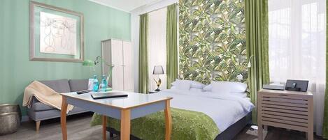 A hotel room with a bed, a desk, a sofa, and a green patterned wall.