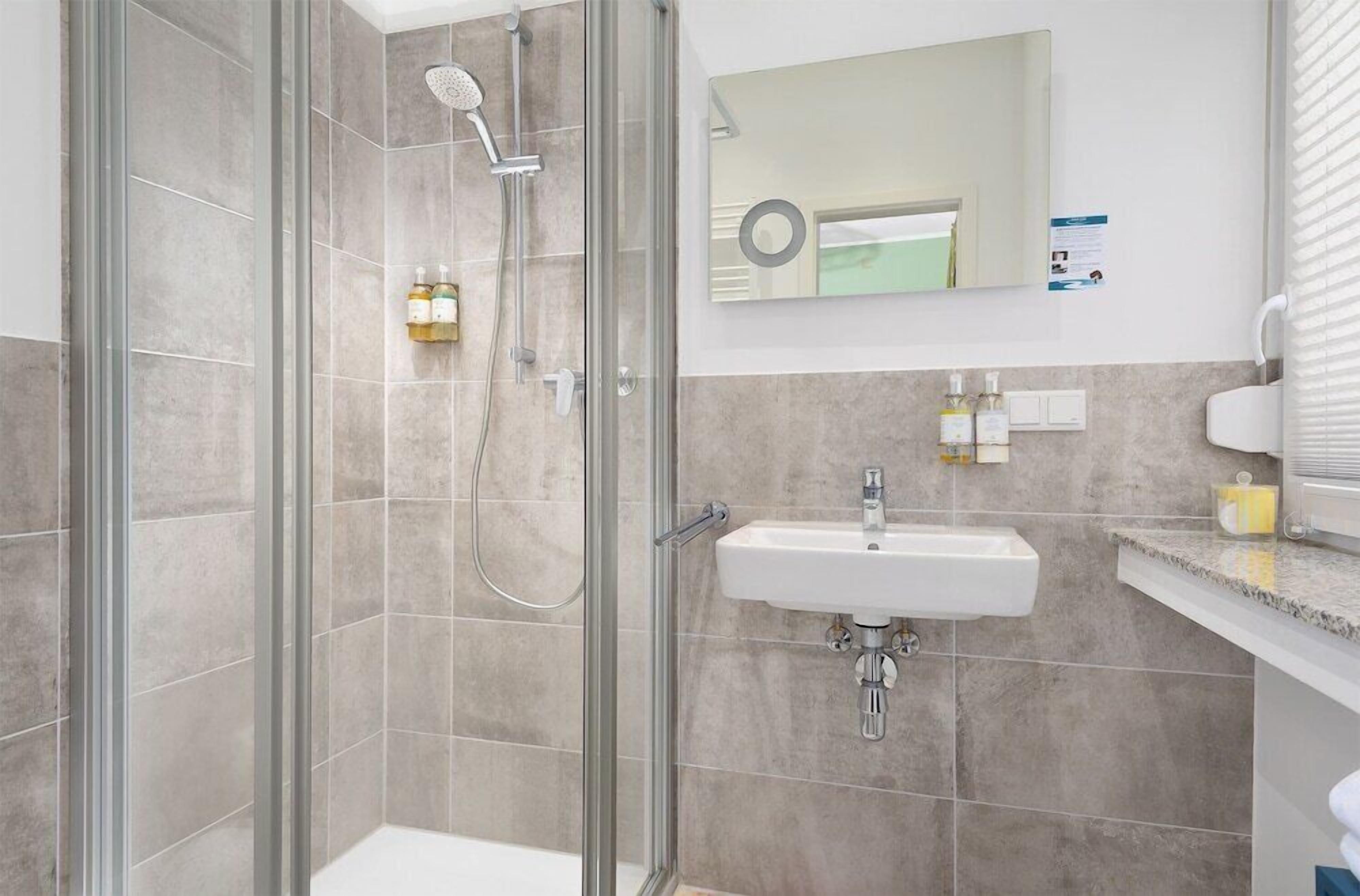 Ein modernes Badezimmer mit einer Duschkabine, einem Waschbecken mit Spiegel darüber und Toilettenartikeln auf der Ablagefläche.