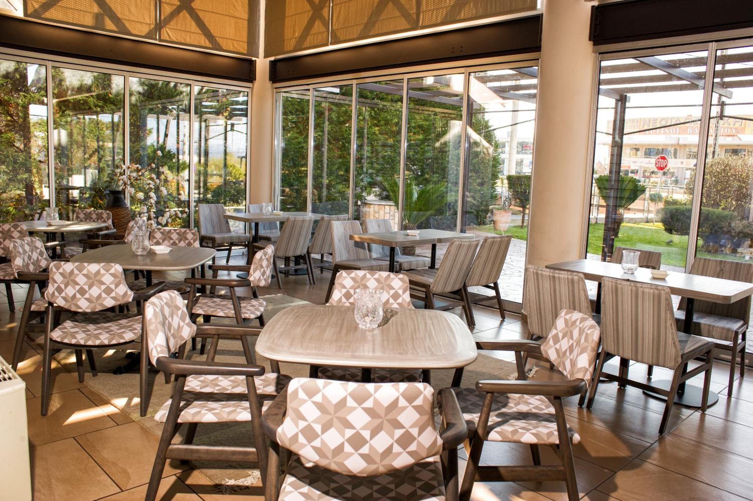 An indoor patio area with multiple tables and chairs, large windows offering views of the outdoors, and a stop sign visible through the window.