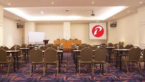 A conference room with a large screen, multiple tables, and chairs arranged for a meeting. - D Primahotel Pattimura Makassar (Makassar)
