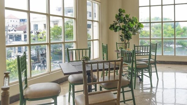 A room with large windows, a dining table with chairs, and a potted plant. - D Primahotel Pattimura Makassar (Makassar)