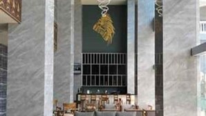 Un hall d’entrée moderne avec un sol en marbre, un ensemble de canapés gris, des tables rondes noires et un luminaire décoratif au plafond.