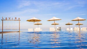 An infinity pool with lounge chairs and umbrellas, and a sign that reads 'LOVINA'. - Lovina Beach Club And Resort (Buleleng)