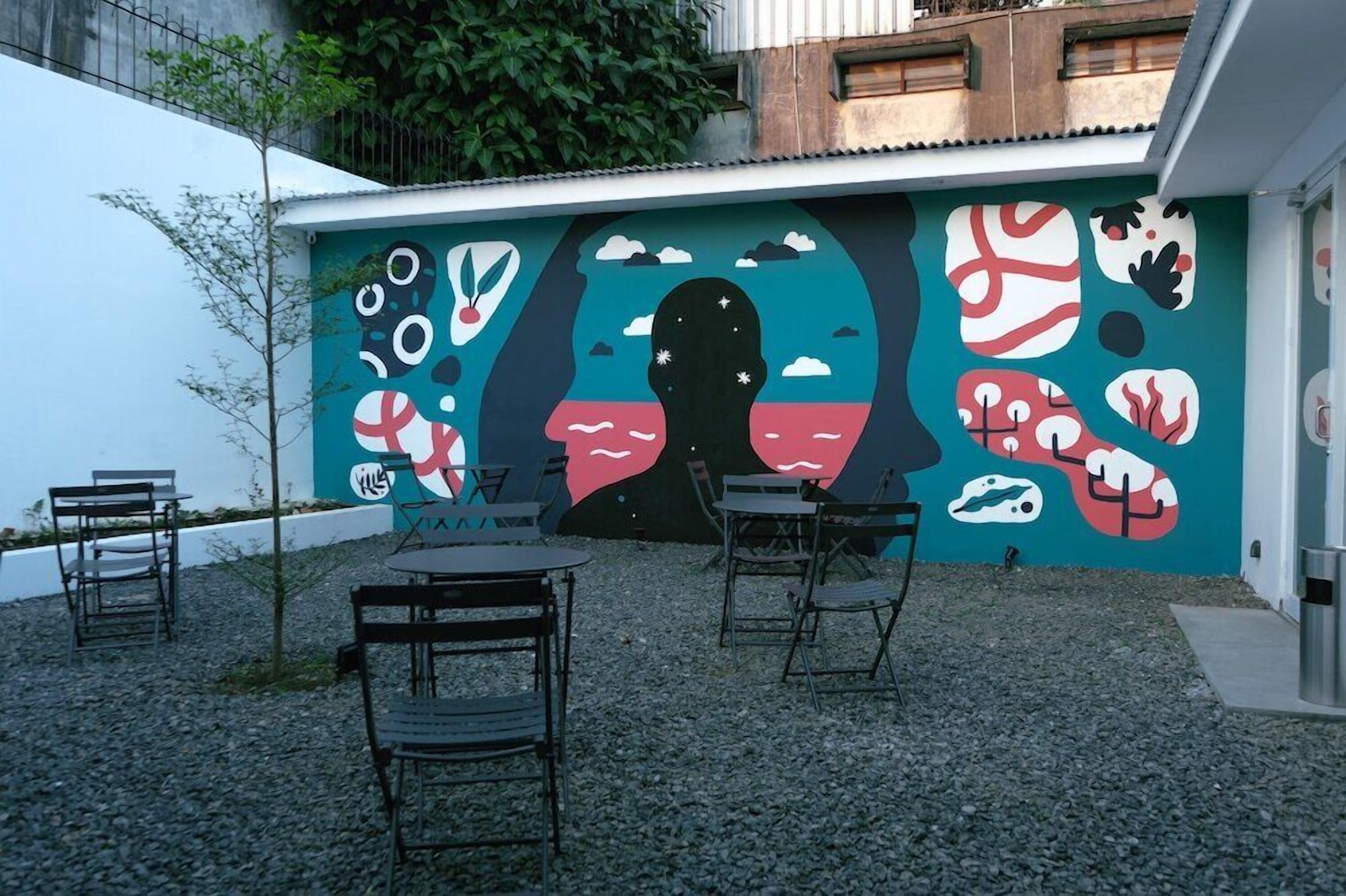 An outdoor seating area with a mural on the wall, tables, and chairs.
