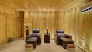 A room with wooden panel walls, two leather sofas, a small table, and a potted plant. - Mystic Valley Spa Resort (Igatpuri)