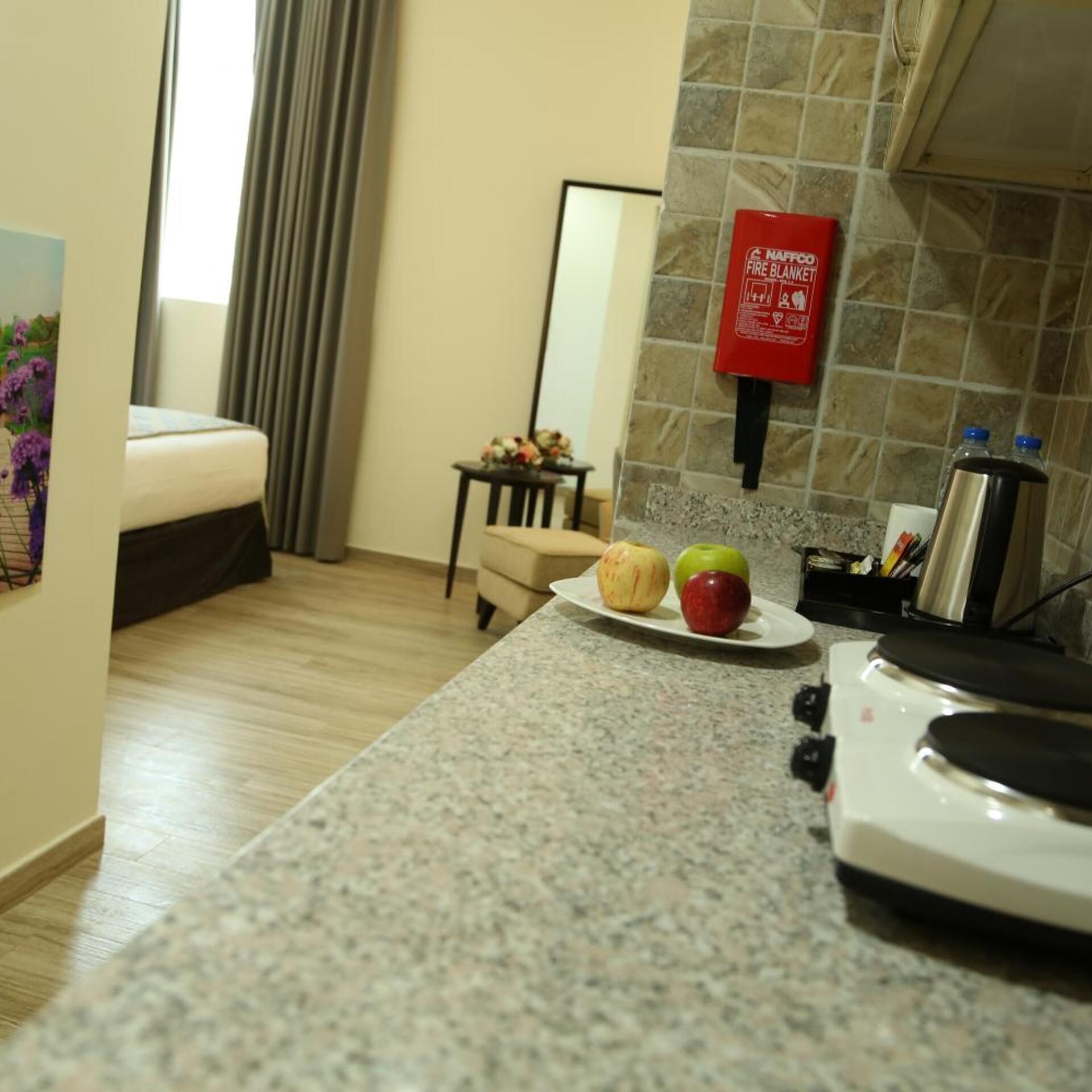 Habitación de hotel con cama, una mesita con una bandeja de frutas, una manta ignífuga y una botella de agua.