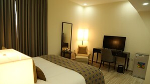 Una habitación de hotel con cama, escritorio, silla, televisor y refrigerador.