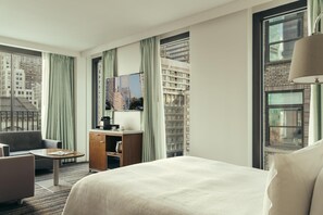 A hotel room with a bed, a desk, a chair, a television, and a window with a city view. - City Gate Hotel (Thermi)