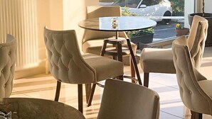 A dining area with round tables and cushioned chairs, a glass coffee table, and a view of the street outside. - City Gate Hotel (Thermi)
