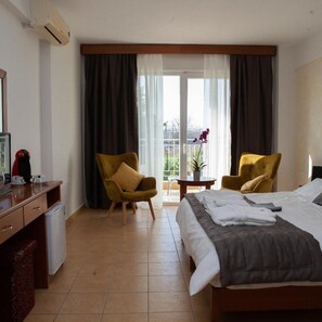 Quarto de hotel com cama, duas poltronas, uma mesa de escritório e máquina de café, além de vista para o exterior.