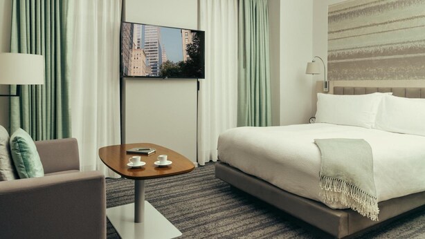 A hotel room with a bed, a TV on the wall, a small table with a cup, and curtains. - City Gate Hotel (Thermi)