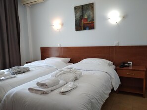 A hotel room with two beds, white linens, neatly folded towels, a wooden headboard, a painting on the wall, and a nightstand with a phone. - City Gate Hotel (Thermi)