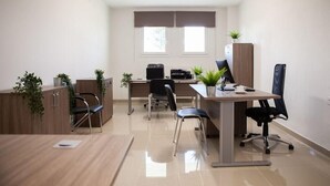 A modern office space with a wooden desk, black office chairs, a printer, and potted plants. - City Gate Hotel (Thermi)