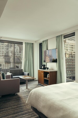 A hotel room with a bed, a desk, a chair, a sofa, and large windows with curtains. - City Gate Hotel (Thermi)